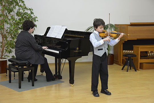 Mladý houslista v doprovodu svého pedagoga na jevišti